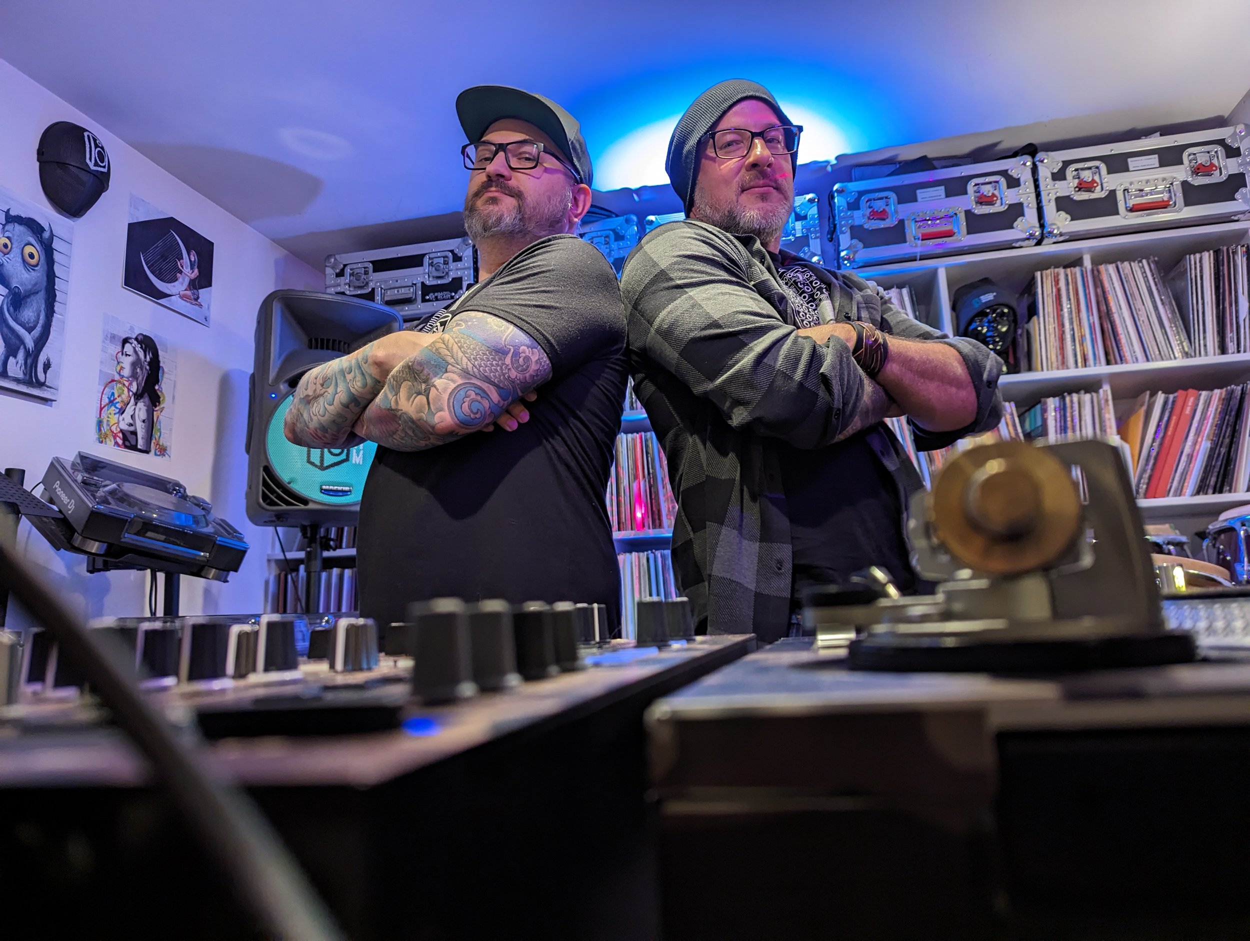Jeremy Linden and Phil Anthony posing back-to-back in studio with vinyl records and equipment visible