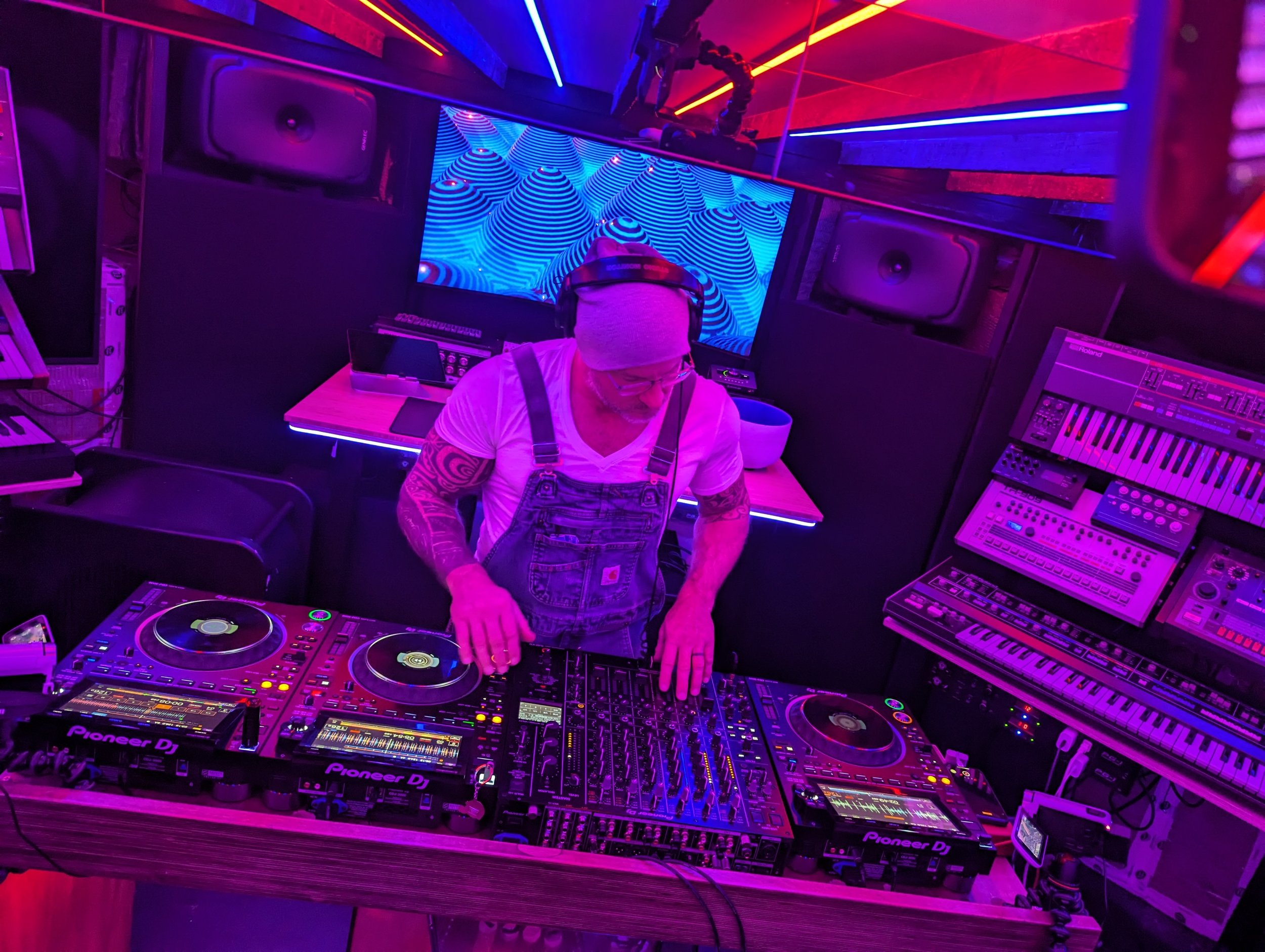 Phil Anthony performing on Pioneer DJ equipment in a studio bathed in pink and purple lighting.