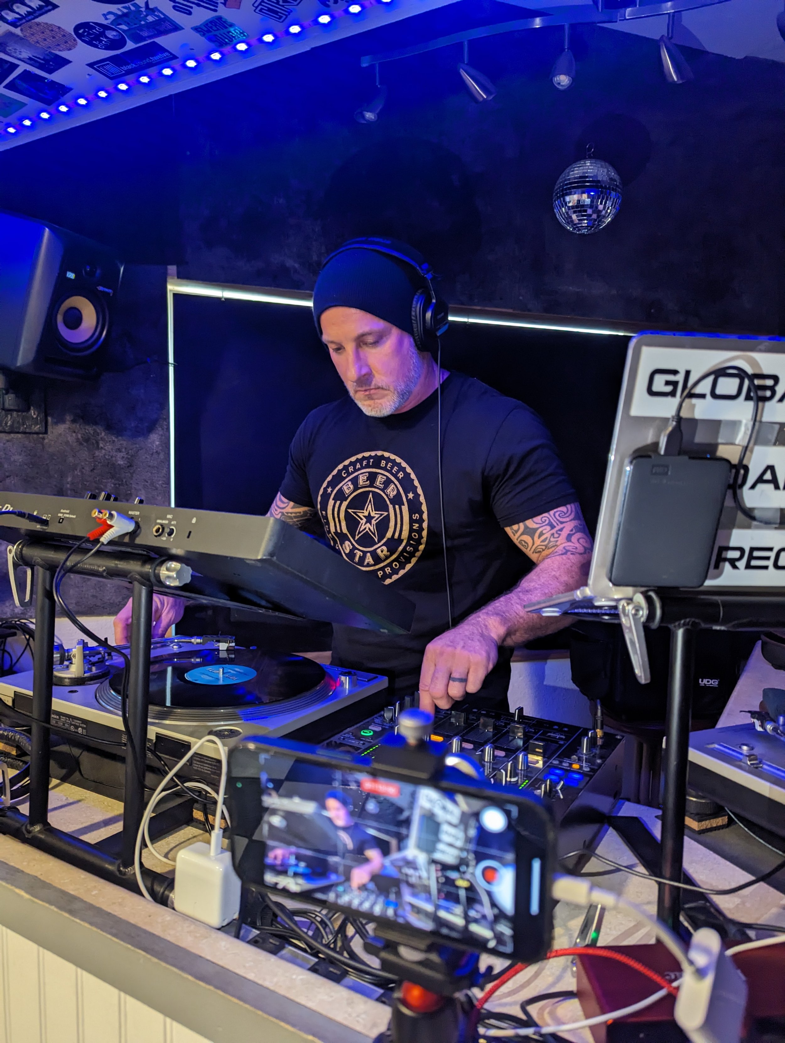 Phil Anthony performing live with turntables and mixer while streaming, lit by blue stage lighting.