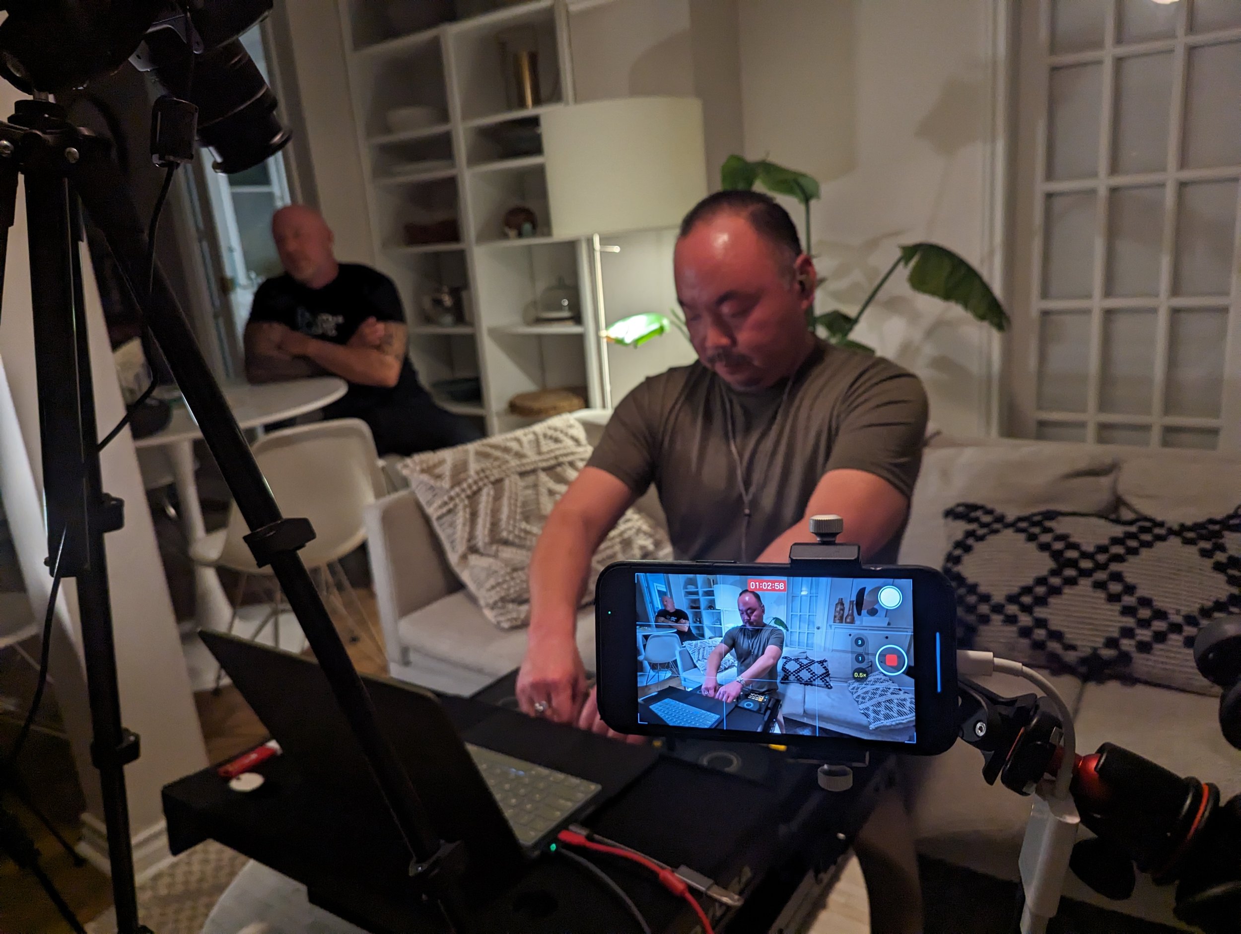 Sang-Do practicing with a portable controller while being filmed for a livestream, with smartphone camera mounted on a tripod.