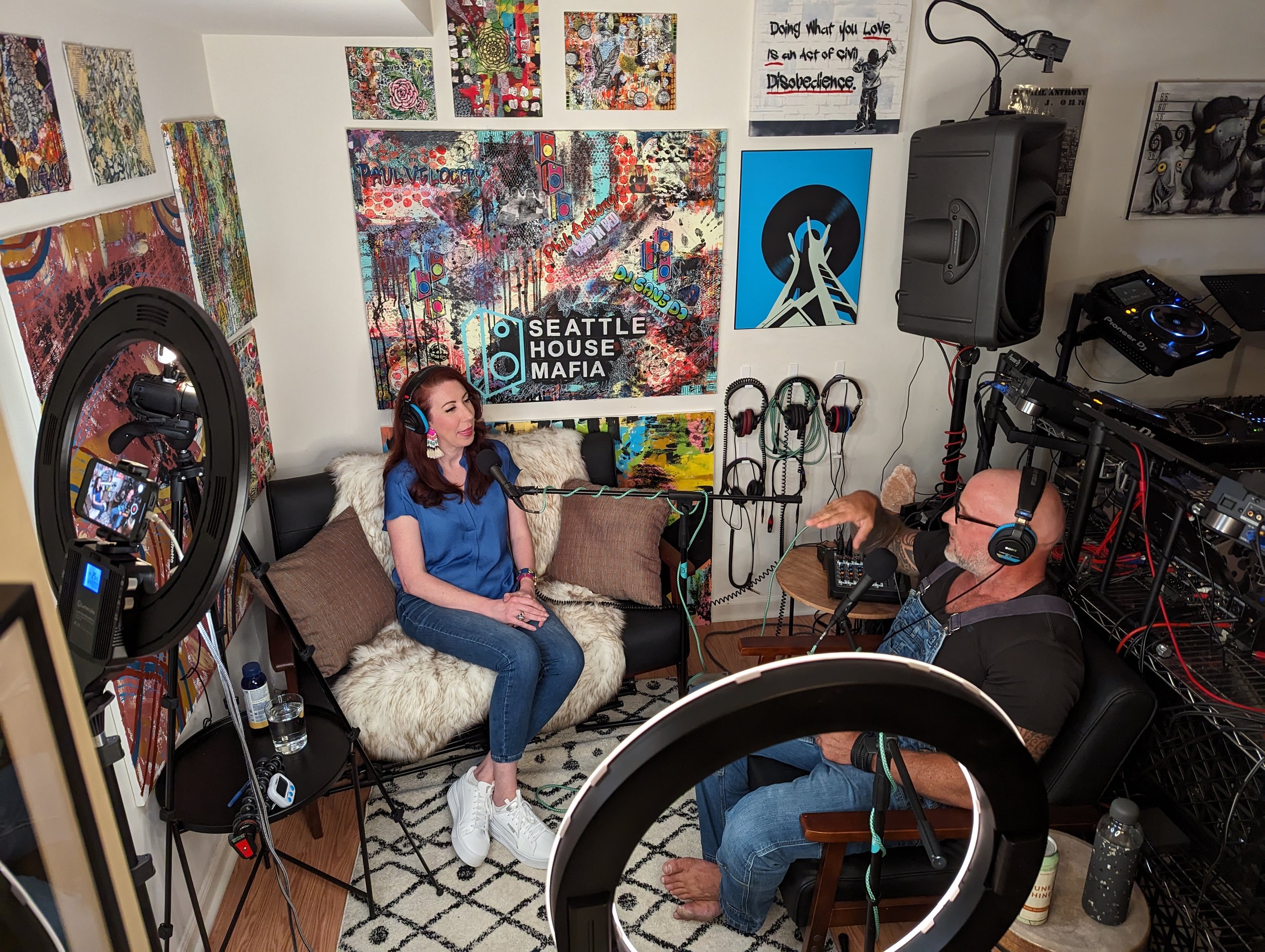 Podcast recording session with Phil Anthony and GriffinGrrl in a home studio decorated with Seattle House Mafia artwork and DJ equipment.