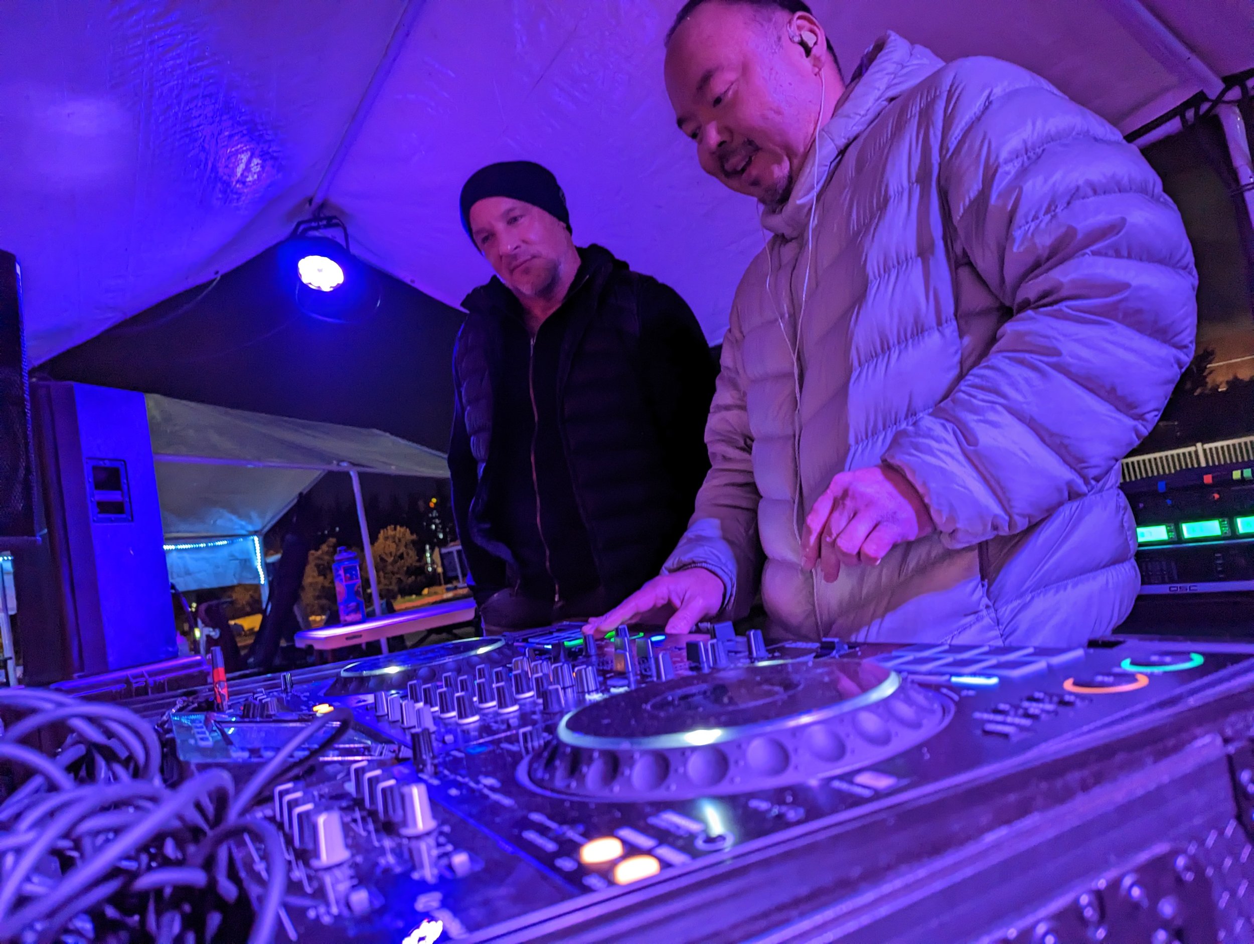 Crowd dancing at a nightclub with DJ booth visible in foreground, illuminated by red and blue lights