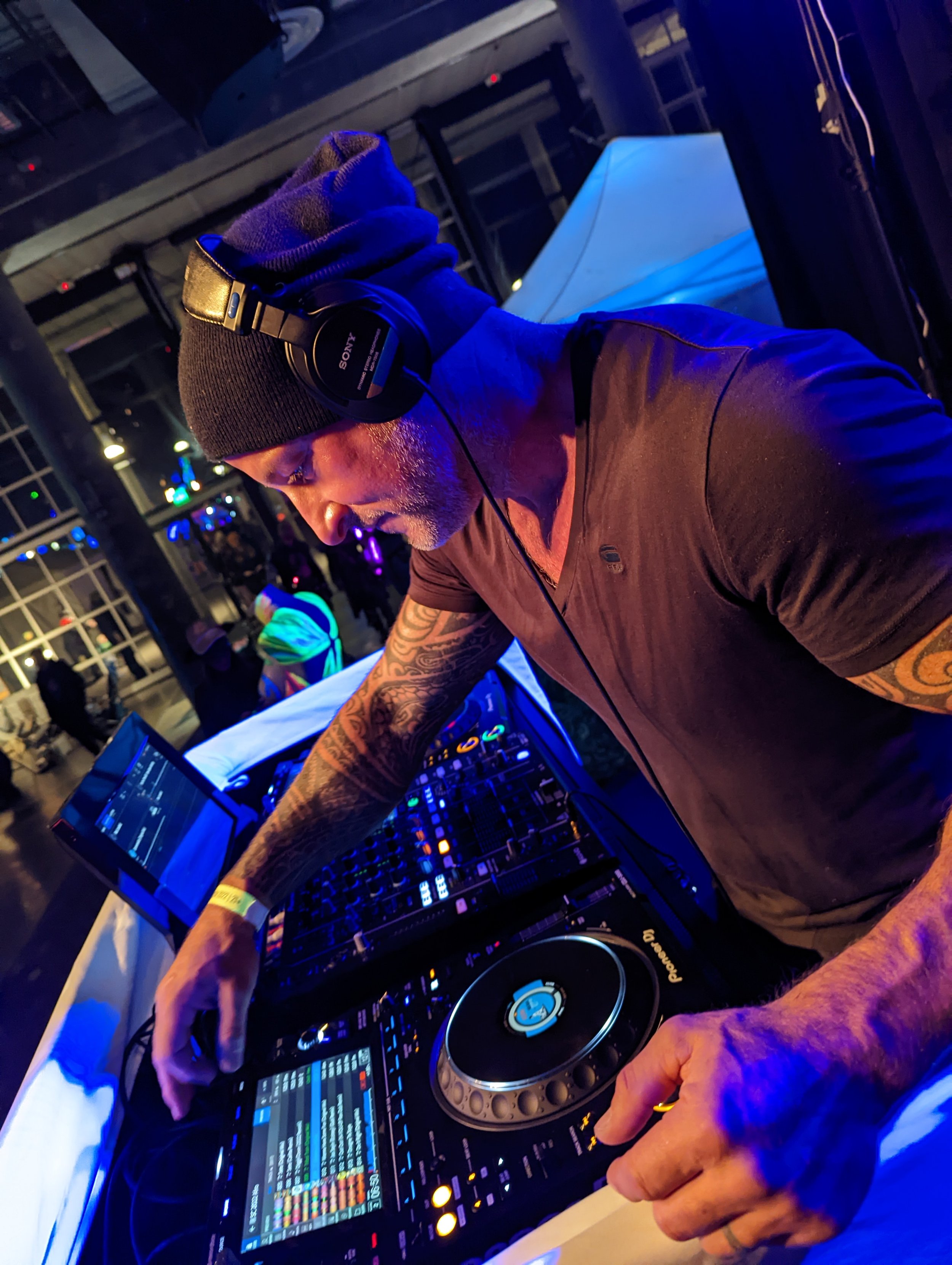 DJ performing in a neon-lit studio with Pioneer DJ equipment and synthesizers visible