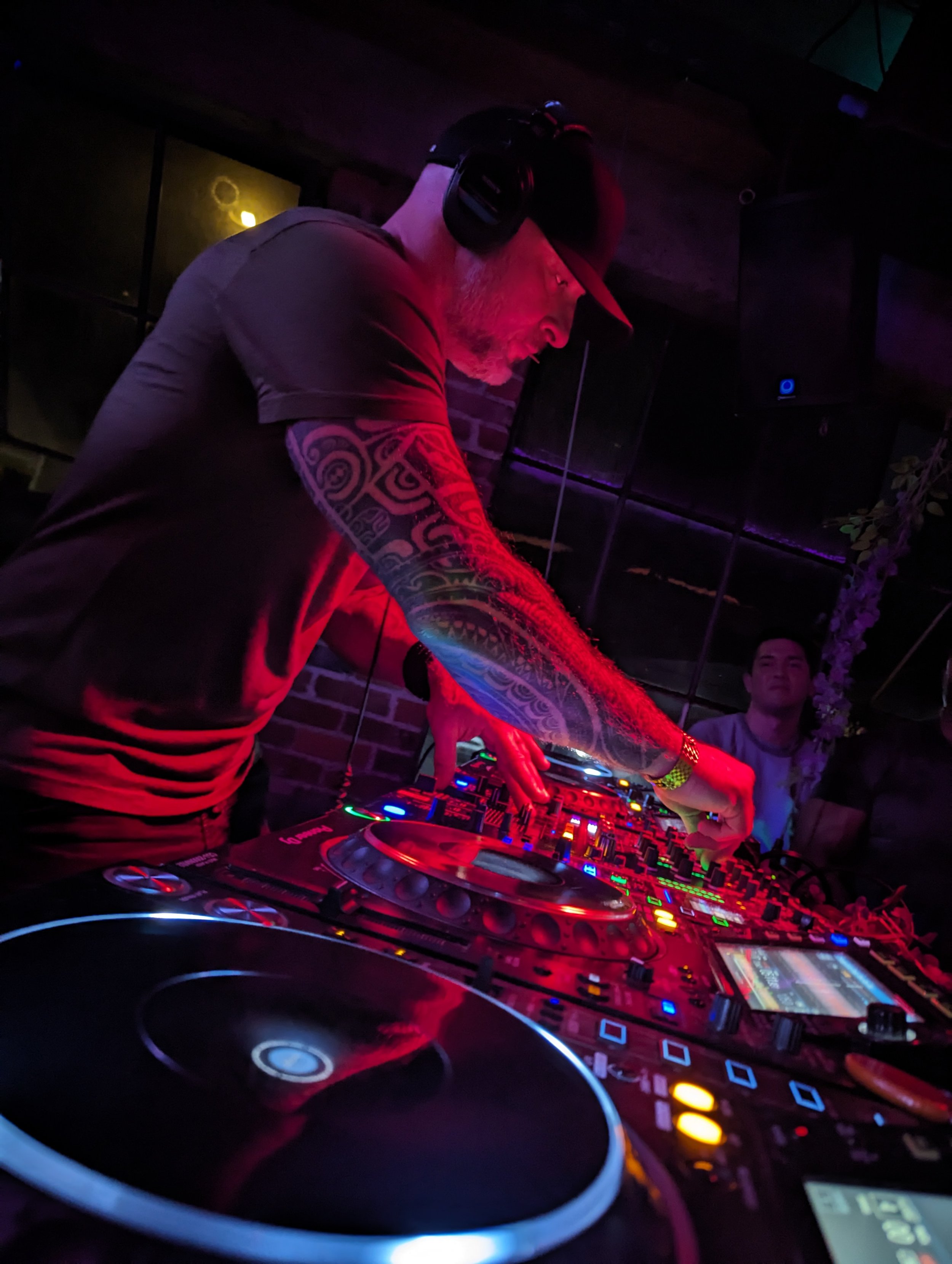 Enthusiastic crowd dancing at a nightclub with DJ booth decorated with purple flowers