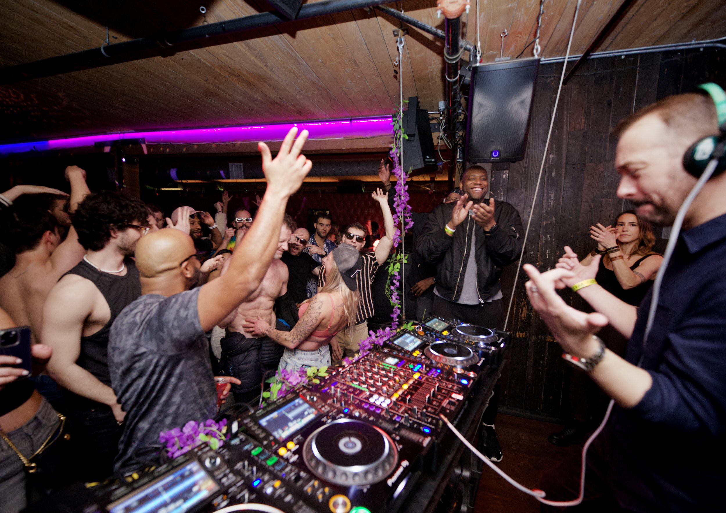 DJ in black shirt with Pioneer CDJ setup surrounded by vinyl record collection
