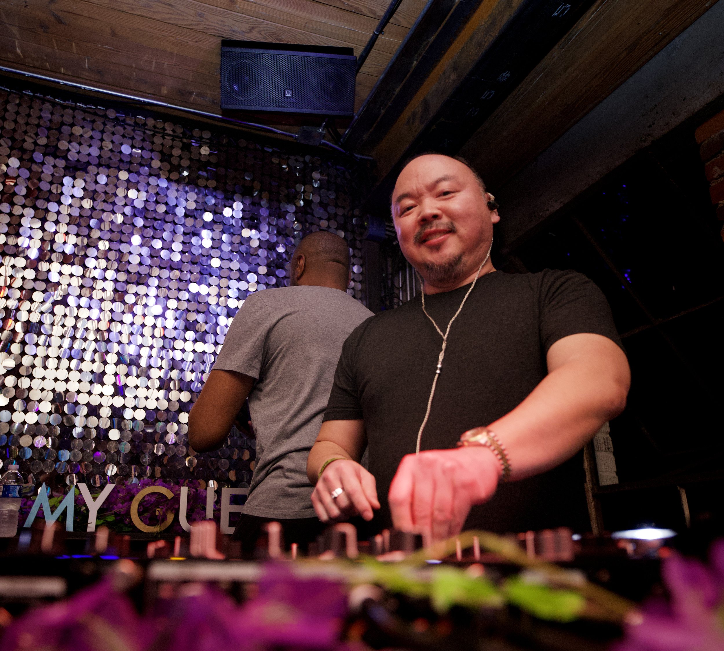Two DJs in a home studio taking a selfie with DJ equipment and LED lighting