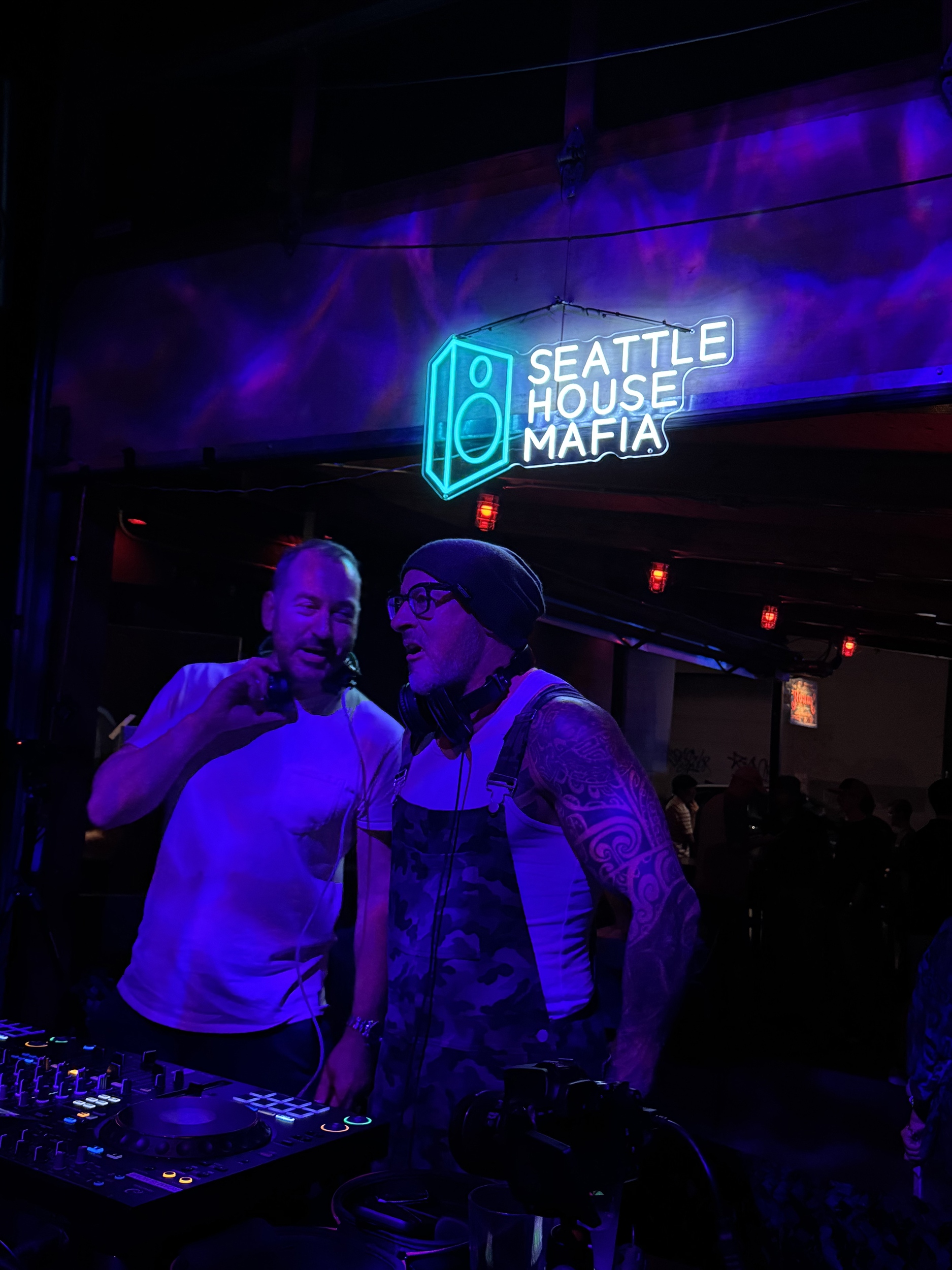 Two Seattle House Mafia DJs behind the decks under the Seattle House Mafia neon sign